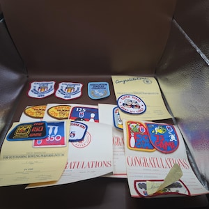 May include: A collection of vintage bowling achievement patches and certificates. The embroidered patches feature colorful designs, bowling pins, and text including California State, Association Singles Champion, and Super Stars I Beat My Coach.