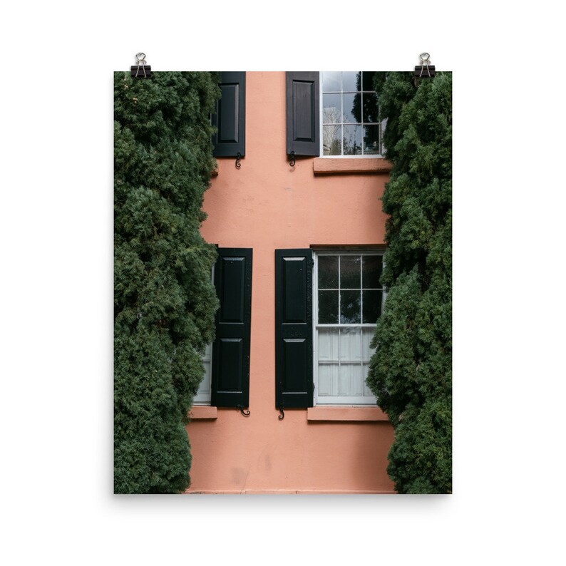 May include: A peach-colored building with black shutters and windows. The building is flanked by two large green bushes.