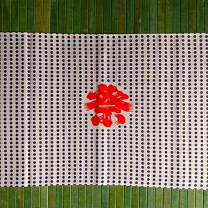 May include: White fabric with a repeating pattern of small blue dots. A red Japanese character is centred on the fabric.