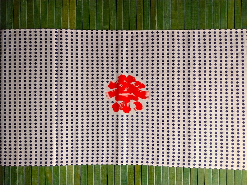May include: White fabric with a repeating pattern of small blue dots. A red Japanese character is centred on the fabric.