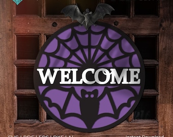 May include: A purple and black round welcome sign with a bat and spiderweb design. The sign says "WELCOME" in white letters.