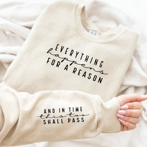 May include: A beige sweatshirt with the text "Everything happens for a reason" on the front and "And in time this too shall pass" on the sleeve.