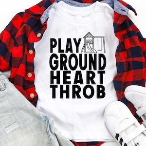 Op de afbeelding: Wit T-shirt met zwarte tekst die "PLAYGROUND HEART THROB" luidt. De tekst is over een zwart-witte illustratie van een speeltuin met een glijbaan en schommels gelegd.