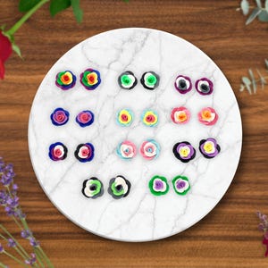 May include: A set of 12 pairs of polymer clay earrings, each pair featuring a different color combination of flowers. The earrings are displayed on a white marble surface.