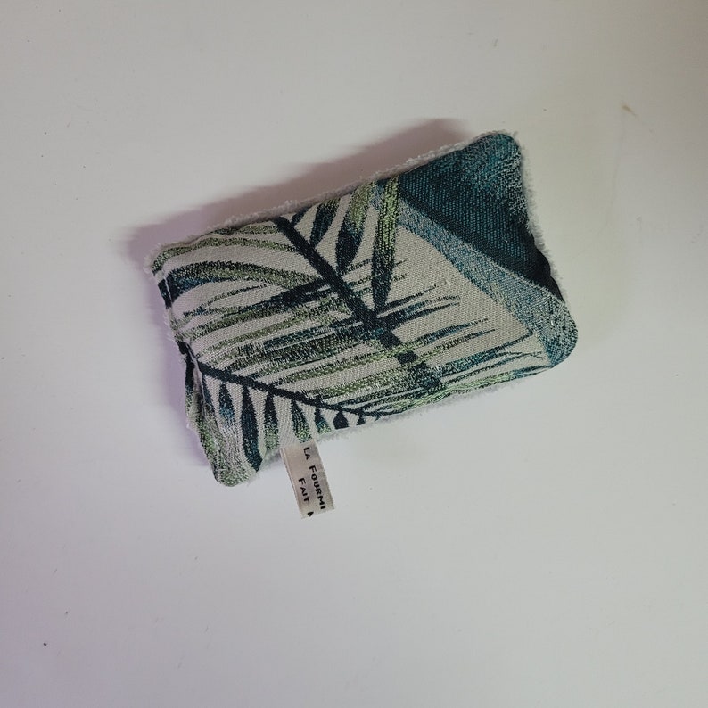 May include: A white and green fabric pouch with a tropical leaf pattern. The pouch has a label that reads "La Fourmi Fait"