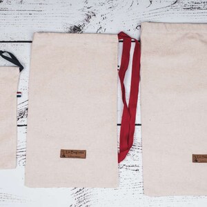 May include: Three beige drawstring bags with different sized black and red drawstrings. The bags have a brown label with the text "La Bagagerie" on them.
