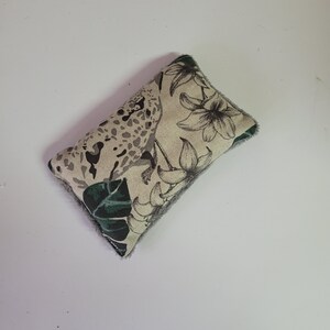 May include: A small, rectangular pillow with a gray and white fabric cover. The fabric features a black and white print of a leopard and tropical flowers. The pillow is filled with a soft, gray material.