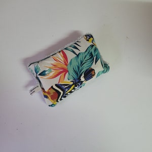 May include: A white fabric pouch with a tropical floral print featuring green leaves, orange, yellow, and blue flowers. The pouch has a white label with the text "REVERSE MAIN" on it.