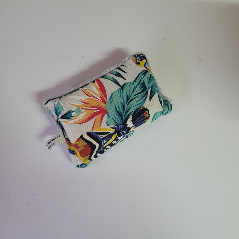 May include: A white fabric pouch with a tropical floral print featuring green leaves, orange, yellow, and blue flowers. The pouch has a white label with the text "REVERSE MAIN" on it.