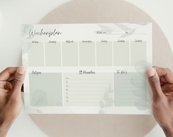 May include: A weekly planner with a light green and white design. The planner has sections for each day of the week, a to-do list, and a notes section. The planner is on a light brown surface.