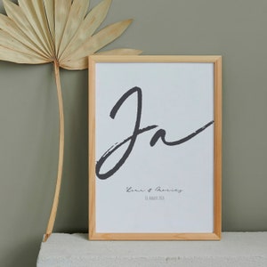 Könnte beinhalten: Ein gerahmter Druck mit einem schwarz-weißen Kalligrafie-Design des Wortes "Ja". Der Druck enthält auch den Text "Lena & Morris" und das Datum "14. August 2026".