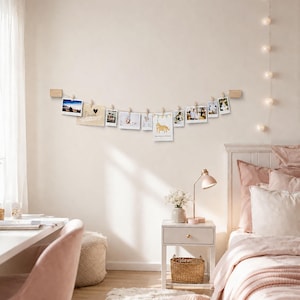 Könnte beinhalten: Ein Fotohalter aus hellem Holz mit einer horizontalen Schnur, die zwischen zwei rechteckigen Wandhalterungen aus Holz gespannt ist. Kleine Holzklammern halten eine Reihe verschiedener rechteckiger Fotos und eine Karte mit dem Wort Danke.