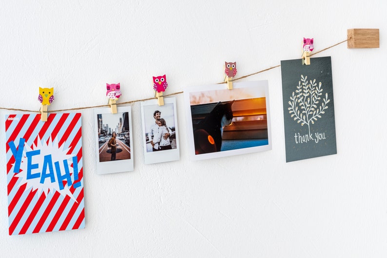 Puede incluir: Una cuerda de fotos y una tarjeta est&aacute;n colgadas en una pared blanca con pinzas de ropa de b&uacute;ho de colores. Las fotos incluyen una pareja, un gato y una calle de la ciudad. La tarjeta dice "gracias".