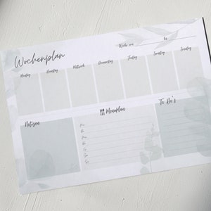 以下が含まれることがあります： グレーと白のカラーリングの週間プランナー。プランナーには、「Wochplan」、「Notizen」、「Mealplan」、「To Do's」のセクションがあります。