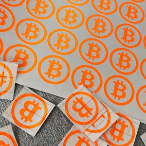Könnte beinhalten: Ein Blatt weißes Papier mit mehreren orangefarbenen runden Aufklebern mit dem Bitcoin-Symbol. Die Aufkleber sind in Reihen und Spalten angeordnet. Es gibt auch mehrere quadratische Aufkleber mit dem Bitcoin-Symbol auf weißem Hintergrund.
