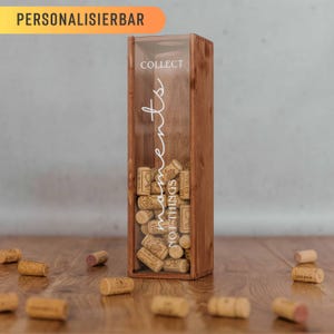 Könnte beinhalten: Eine Holzkiste mit einer durchsichtigen Glasfront, gefüllt mit Weinkorken. Die Kiste trägt den Aufdruck "COLLECT NOT THINGS MOMENTS" auf der Vorderseite.