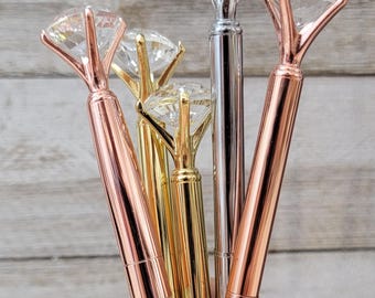 May include: Five diamond-shaped pens with clear rhinestones. The pens are in different colors: silver, rose gold, and gold.