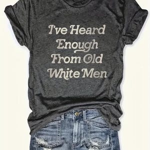 Puede incluir: Una camiseta gris oscuro con el texto "I've Heard Enough From Old White Men" impreso en blanco.