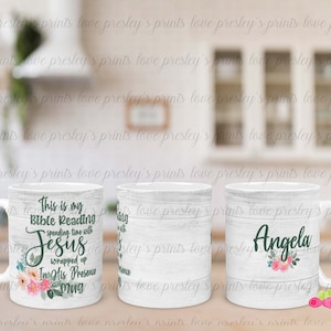 Pode incluir: Duas canecas de cerâmica branca com um padrão de grão de madeira. Uma caneca tem um design floral e o texto "This is my Bible Reading spending time with Jesus wrapped up In His Presence Mug". A outra caneca tem um design floral e o nome "Angela" em texto verde.