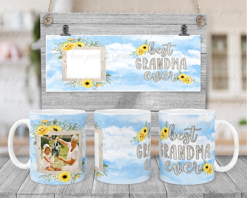 Puede incluir: Dos tazas blancas con nubes de acuarela azul y blanca y girasoles amarillos. Las tazas tienen un marco de fotos con una imagen de una abuela y una nieta. Las tazas tienen el texto "la mejor abuela del mundo" en ellas. Un letrero con el mismo dise&ntilde;o y texto est&aacute; en el fondo.