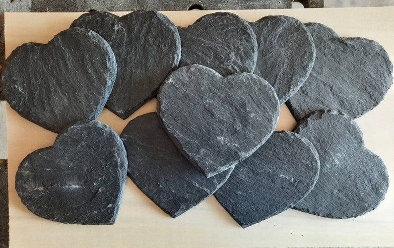 May include: A set of 10 black heart-shaped slate coasters. The coasters are made of natural slate and have a rustic, handmade look.