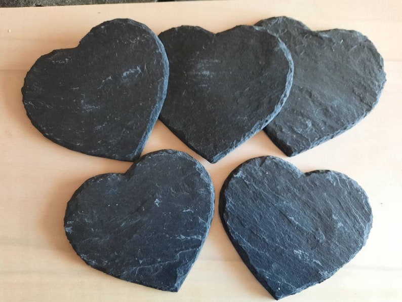 May include: Five black heart-shaped slate coasters. The coasters are made of natural slate and have a rustic, uneven texture.