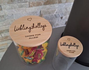 May include: Two glass jars with wooden lids. The lids are engraved with the words "Lieblingskollege" and "DANKE FÜR ALLES!" in black script, with a small heart. One jar is filled with colorful wrapped candies.