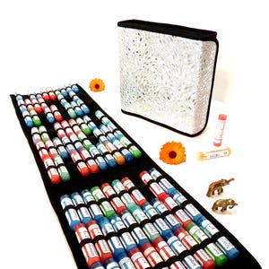 May include: A black, open, zippered case with multiple rows of small, colorful vials. The vials are labeled with white text and held in place by black elastic bands. A silver and white patterned case is also present, along with orange flowers and small brass elephant figurines.