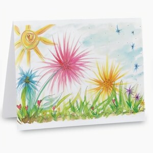 May include: A blank greeting card featuring a watercolor painting of a sunny day. The artwork includes a yellow sun, colorful flowers in pink, blue, and yellow, green grass, and a light blue sky with stars. The card is white.