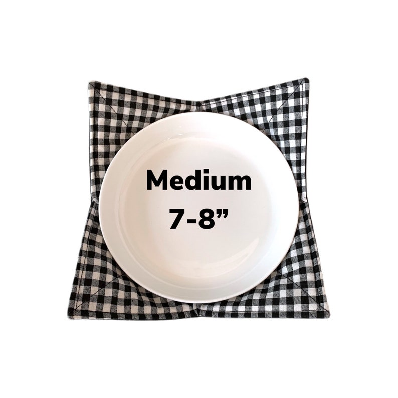 May include: Black and white checkered fabric dish mat with a white ceramic plate in the center. The plate is 7-8 inches in diameter and the text "Medium 7-8" is printed on the plate.
