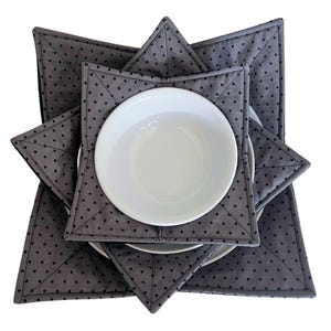 K&ouml;nnte beinhalten: Set aus drei grauen und schwarzen gepunkteten, gesteppten Sch&uuml;sseluntersetzern. Die Untersetzer sind sternf&ouml;rmig und &uuml;bereinander gelegt. Eine wei&szlig;e Sch&uuml;ssel befindet sich in den Untersetzern.
