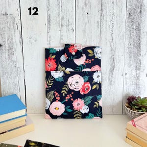 May include: A rectangular fabric sleeve featuring a dark navy blue background with a floral pattern of pink, white, and red roses, green leaves, and gold sprigs. The sleeve has a top flap closure secured with a small white snap button.
