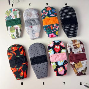 May include: A collection of eight oven mitts with various patterns. Designs include cacti, floral, polka dots, chili peppers, owls, and wine-themed graphics. Each mitt has a contrasting fabric band.