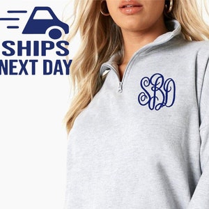 May include: A light gray quarter-zip pullover sweatshirt featuring a dark blue embroidered monogram on the left chest. The monogram consists of the letters S, B, and D in a decorative, interlocking script font style.