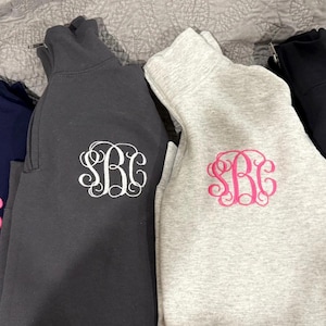 Könnte beinhalten: Zwei Sweatshirts mit Stehkragen, eines ist grau mit einem rosafarbenen Monogramm "SRC" und das andere ist schwarz mit einem weißen Monogramm "SRC".