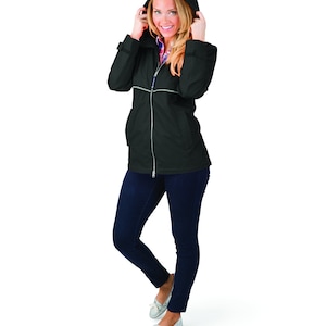May include: A black hooded rain jacket with a zipper closure. The jacket has a reflective trim along the zipper and pockets. The model is wearing blue jeans and white sneakers.