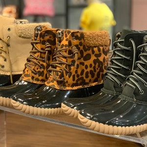 Op de afbeelding: Vier paar dames winterschoenen met verschillende patronen. De laarzen zijn zwart met een bruine rubberen zool en hebben veters. Een paar is beige, een paar is luipaardprint en twee paar zijn zwart met een grijze bontkraag.