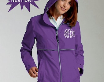 May include: A purple rain jacket with a hood and a white monogram on the front. The jacket has a zipper closure and two pockets.