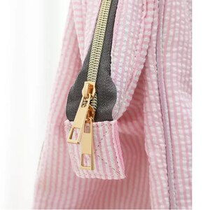 May include: Close-up of a pink and white striped zipper pull on a bag. The zipper pull is gold metal with a gray zipper tape.