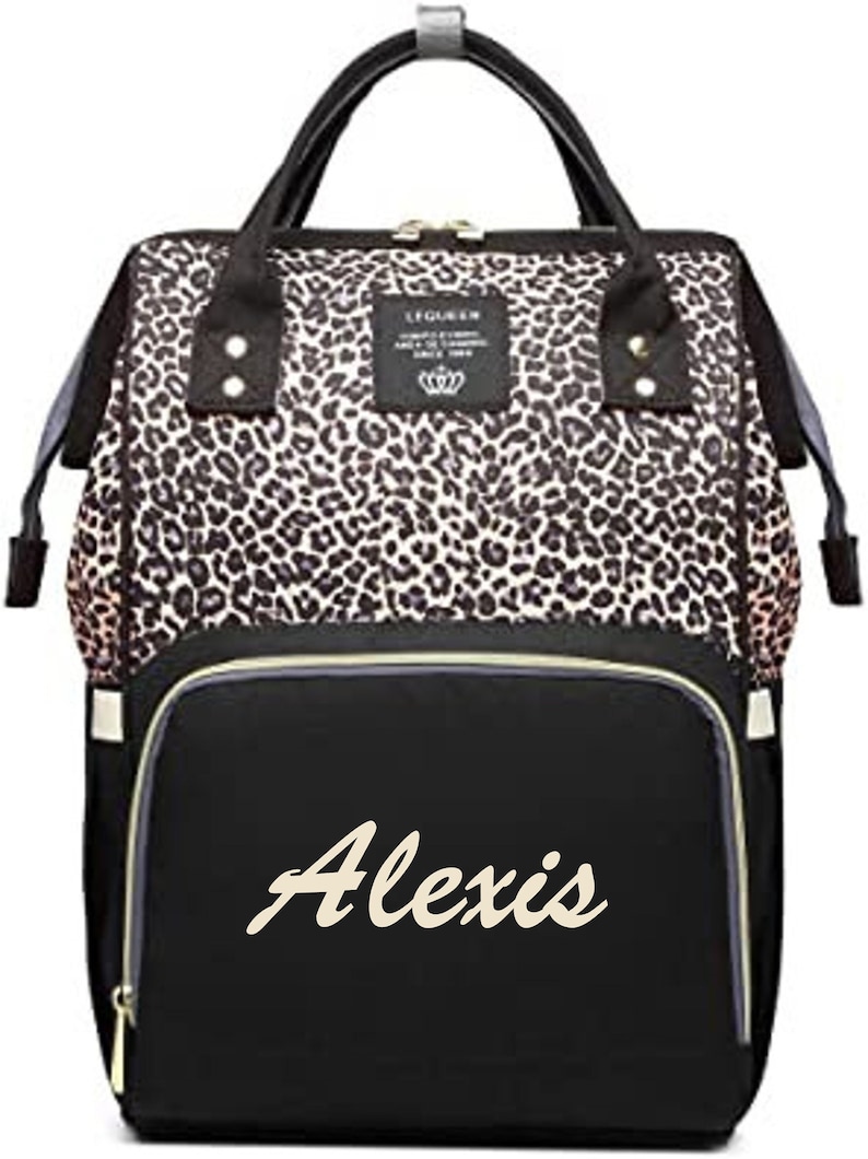 Pu&ograve; includere: Una borsa per pannolini nera e marrone con stampa leopardata e una tasca nera con cerniera sul davanti. La tasca &egrave; ricamata con il nome "Alexis" in color crema.