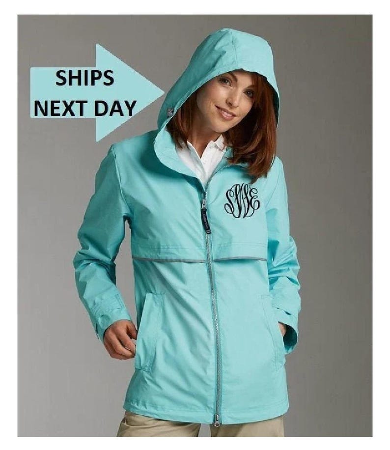 May include: A light blue hooded jacket with a zipper closure and a monogrammed design. The jacket has two pockets and a reflective strip on the front.