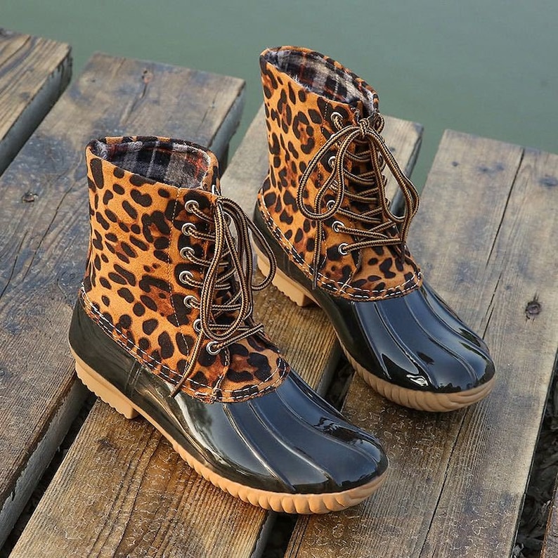 Op de afbeelding: Een paar zwarte en bruine eendenschoenen met luipaardprint en veters. De schoenen hebben een zwarte rubberen zool en een bruine su&egrave;de bovenkant.