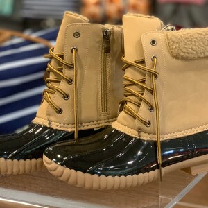 Op de afbeelding: Een paar bruine duck boots met zwarte rubberen zolen en bruine veters. De laarzen hebben een imitatiebontvoering rond de bovenkant.