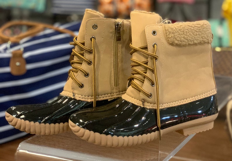 Op de afbeelding: Een paar bruine duck boots met zwarte rubberen zolen en bruine veters. De laarzen hebben een imitatiebontvoering rond de bovenkant.