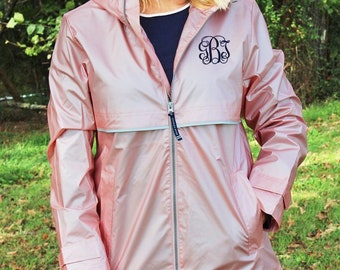 May include: A pink rain jacket with a silver zipper and a white stripe across the chest. The jacket has a hood and two pockets. The jacket is monogrammed with the letters "BSB" in black.