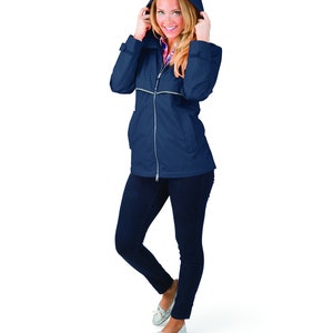 May include: A navy blue hooded jacket with a zipper closure and reflective piping. The jacket is worn by a person with blonde hair and is standing on a white background.