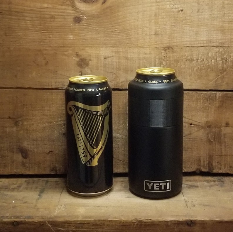 May include: A black Yeti Rambler with the Yeti logo and the text "poured into a glass - best enjoyed" in gold lettering next to a black can of Guinness beer with gold lettering that says "ESTD 1759" and "poured into a glass".