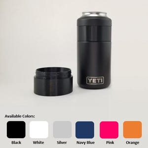 May include: A black YETI can cooler with a silver top and a separate black base. The cooler is cylindrical and has the YETI logo on the front. Available colors include black, white, silver, navy blue, pink, and orange.