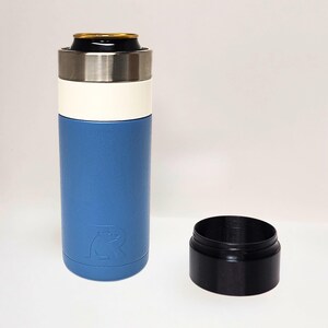 May include: A blue and white insulated beverage holder with a stainless steel rim, holding a can. A separate black base sits beside it. The holder features a bear logo.
