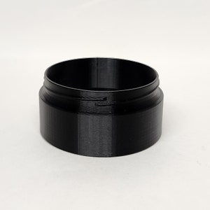 May include: A black, cylindrical container with a wide opening and a slightly raised rim. The container has a smooth, matte finish and appears to be made of plastic. The design is simple and functional, suitable for storing small items.
